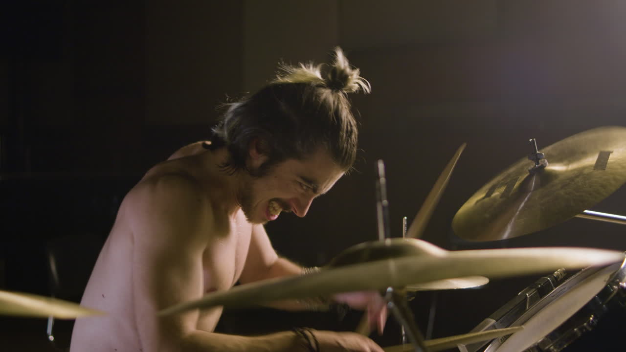 baterista masculino sin camisa enérgico con barba tocando la batería