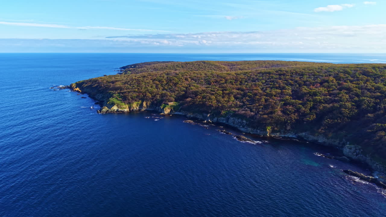 Scogliere costiere abbracciano le serene acque blu di una baia isolata sotto un cielo limpido nella luce dorata del tardo pomeriggio.