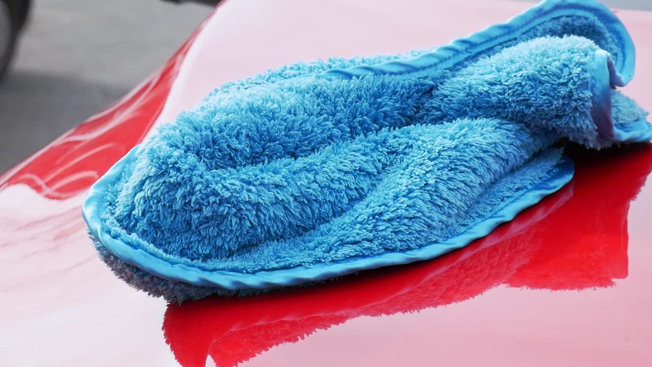 Super soft blue microfiber towel on a red car hood being pick up - extreme close up