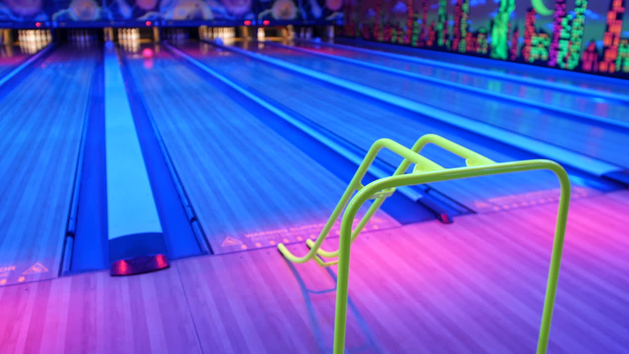 um jogador de boliche segurando uma bola de boliche laranja, pronto para colocá-la em uma rampa em uma pista de boliche iluminada a neon