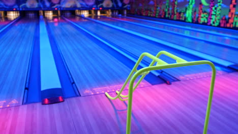 a bowler holding an orange bowling ball, ready to place it on a ramp at a neon-lit bowling alley