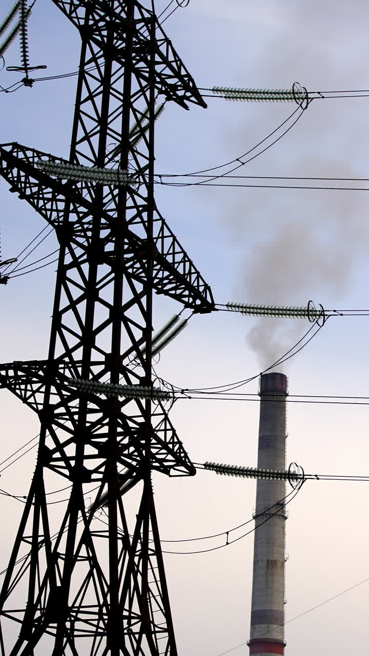 High-voltage towers and pipes of power station with smoke. Chemical emissions from industry next to transmission lines on sky background. Vertical video