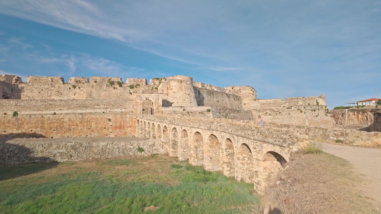 Bir turist, Yunanistan'daki muhteşem Methoni Kalesi'ne giden taş kemerli deniz hendek köprüsünden geçiyor.