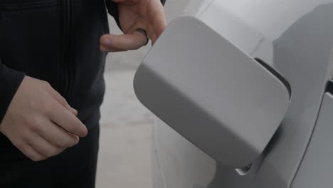 gasolinera hombre caucásico blanco con anillo de bodas llenando coche plateado presionando y abriendo la tapa del tanque de combustible y gesticulando con las manos