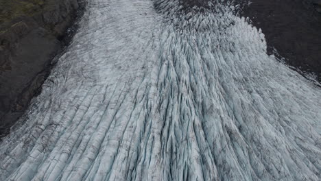 reverse flyover above deep crevasses in large iceland glacier, dirty with silt