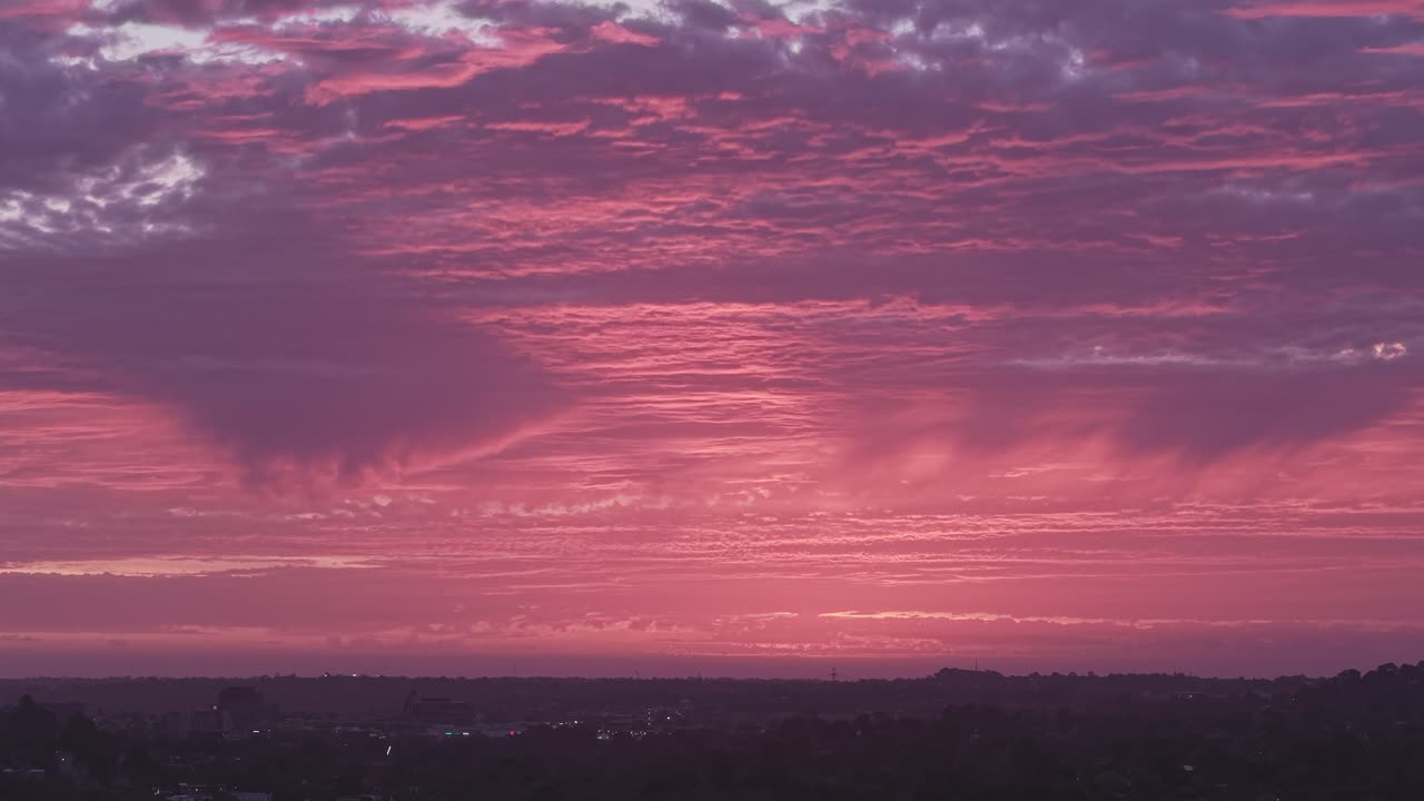 Breathtaking aerial shot captures a vibrant, colorful Australian sunset over cityscape. The sky bursts with pink and purple hues, creating a dramatic and serene atmosphere. No people visible
