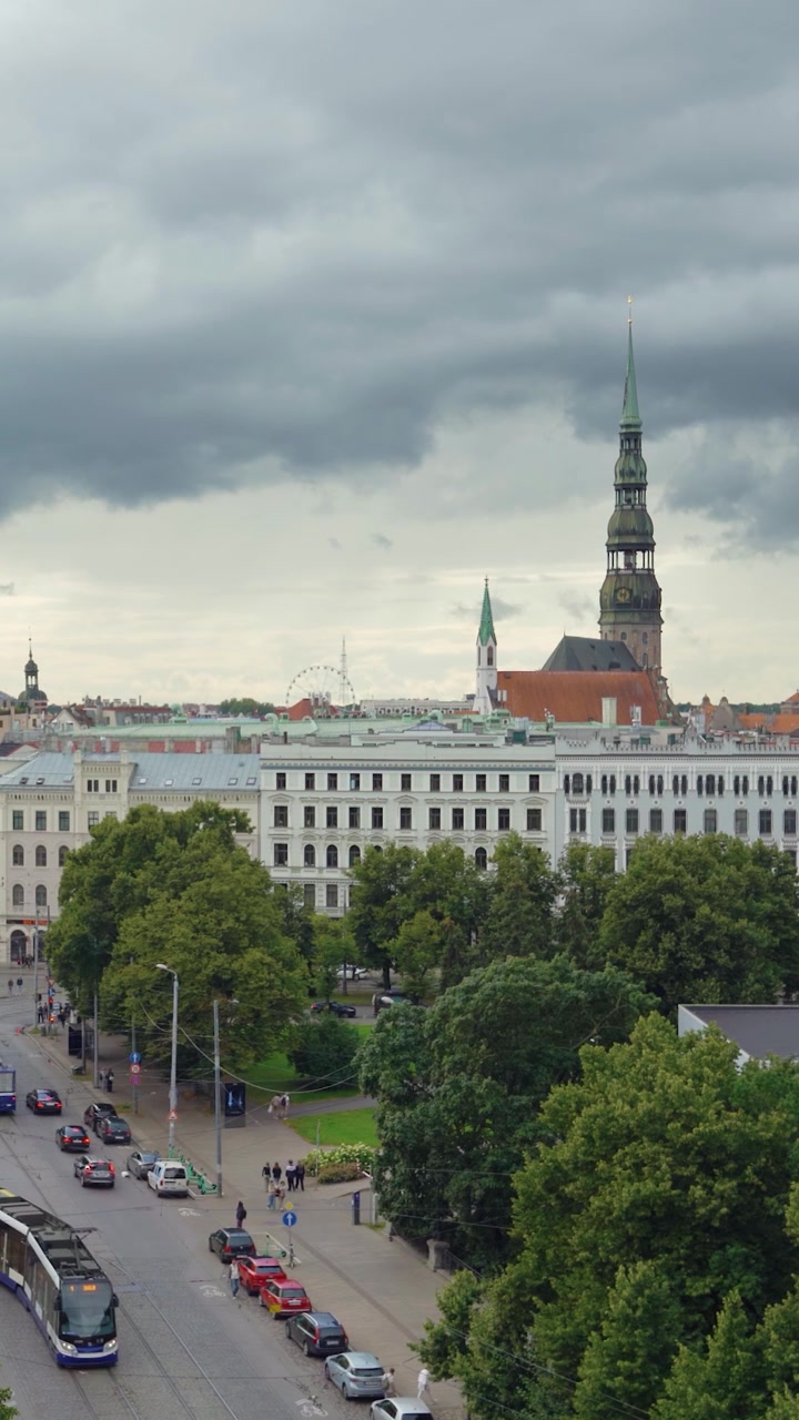 Vista verticale del paesaggio urbano della Città Vecchia di Riga con la guglia della Chiesa di San Pietro, un tram e drammatiche nuvole temporalesche sopra.