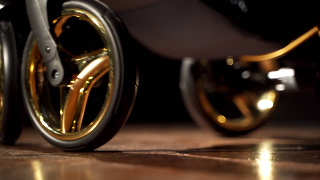 Shiny wheels being turned and spark in the light. Black baby pram pushed in dark room. Close up.