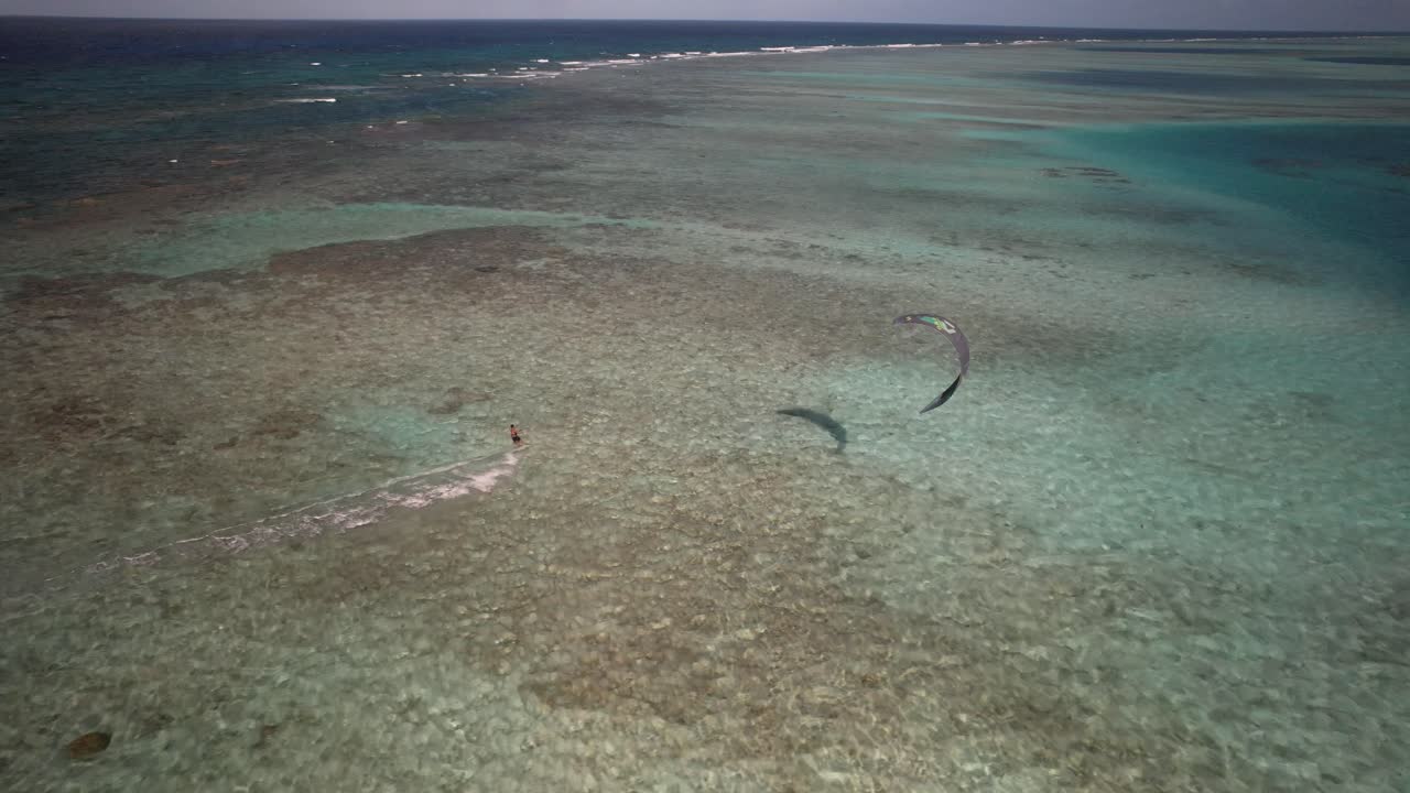 A kite surfer glides over the clear, shallow waters of Cayo Vapor on a sunny day