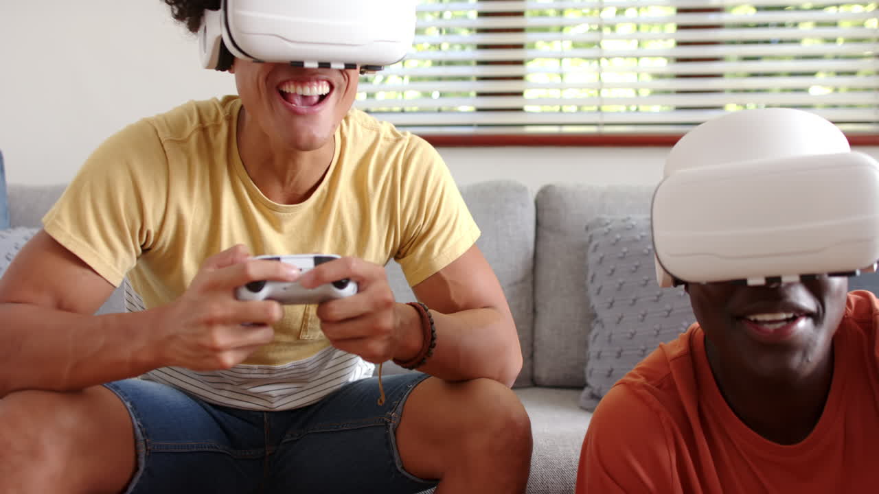 Playing video games with VR headsets, two multiracial male friends enjoying time together, at home