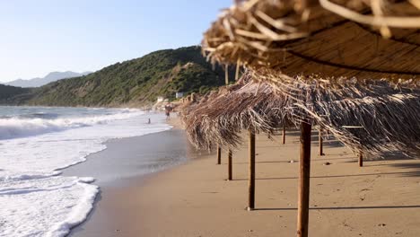 Sonnenschirme-Am-Strand-Mit-Schäumenden-Wellen-Und-Wind,-Der-In-Zeitlupe-Weht