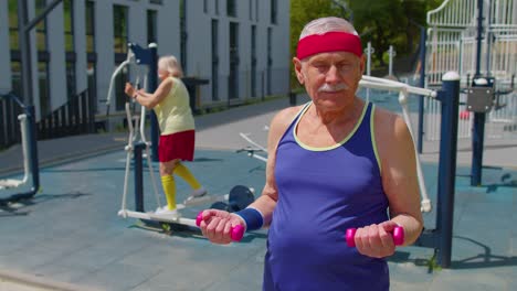 Senior-man-grandfather-doing-active-training-weightlifting-exercising-with-dumbbell-on-playground