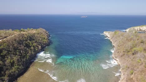 Aerial-view-of-Atuh-beach-on-Nusa-Penida,-Indonesia-on-a-sunny-day-and-with-crystal-blue-water-hitting-the-rock-formations