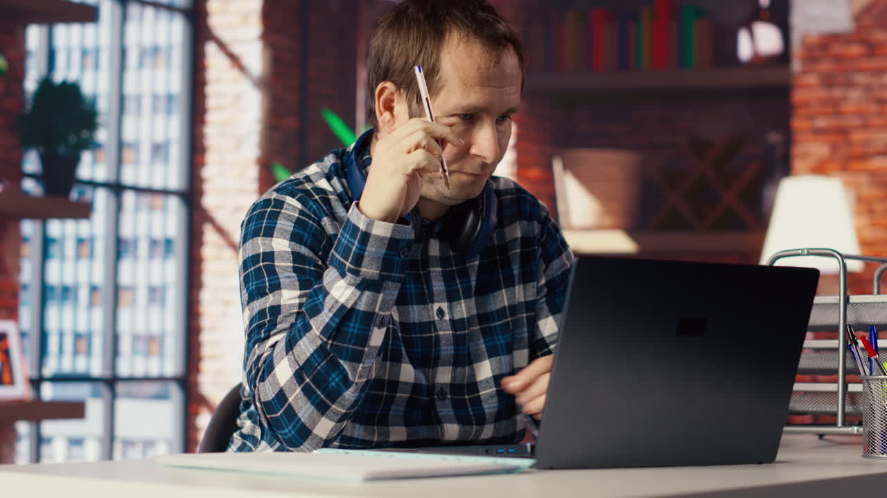 hombre estresado en la oficina de casa rascándose la cabeza con una pluma, sintiéndose sobrecargado de trabajo