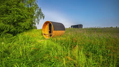 barrel sauna in a grassy field time-lapse of the morning fog fading away to a bright sunny day