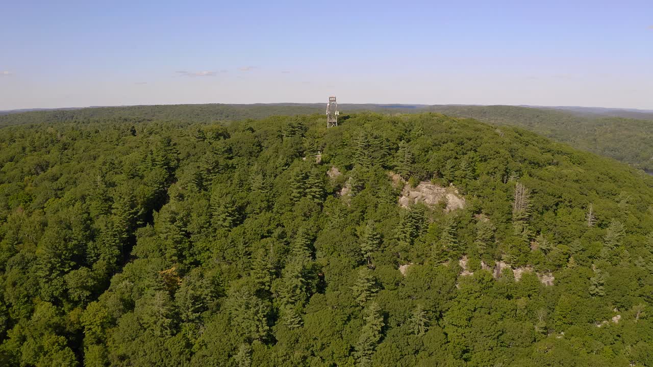 Drone shot approaching lookout tower on hilltop in the middle of Ontario forest