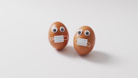 video of eggs with eyes and face masks on a white surface