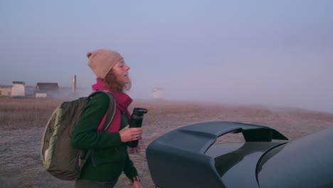 woman with backpack near car in foggy morning