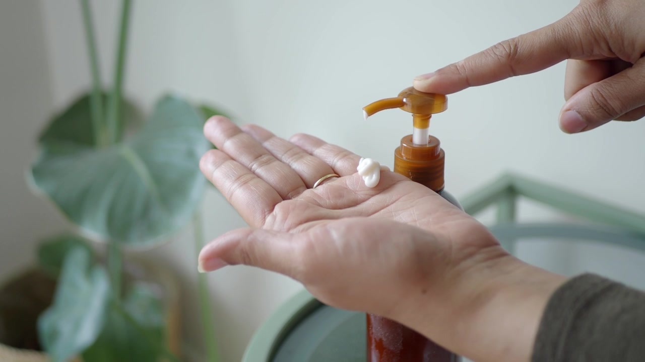 Persona aplicando loción blanca en la mano desde una botella marrón