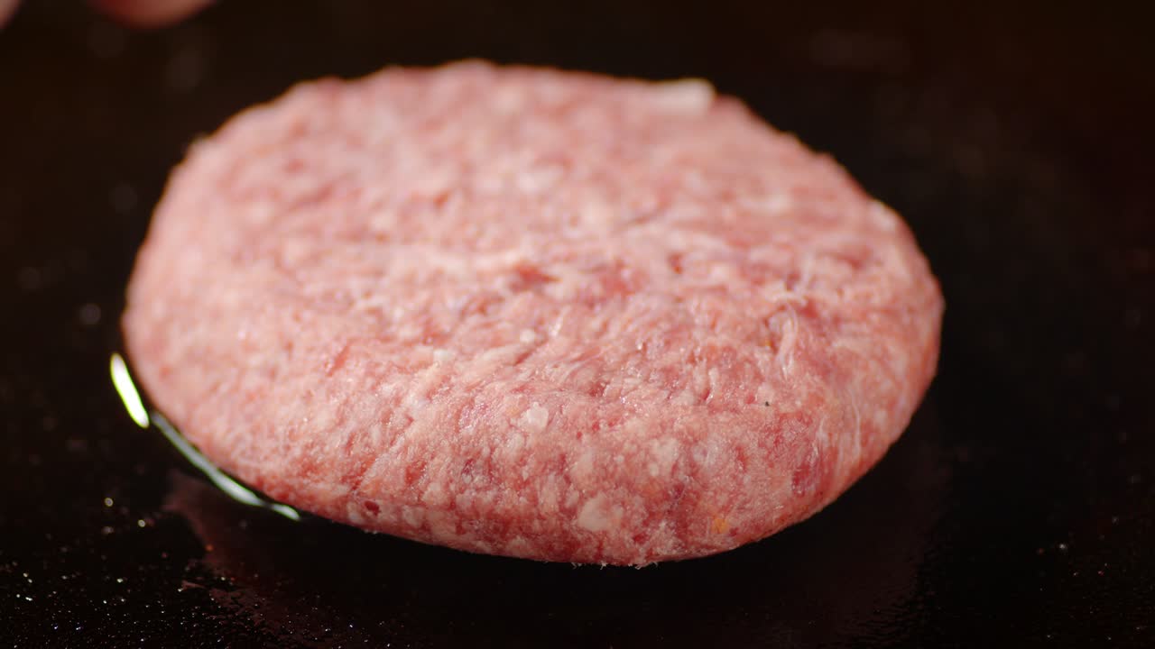 The men's hand puts raw burger meat in the pan.
