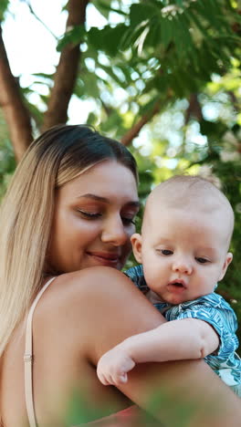 mother and her infant spending time outdoors in summer. happy smiling mom touching her baby tenderly. vertical video