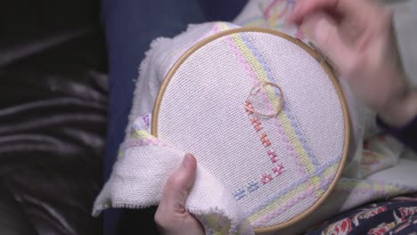 over the shoulder shot of a woman cross-stitching a pattern onto material