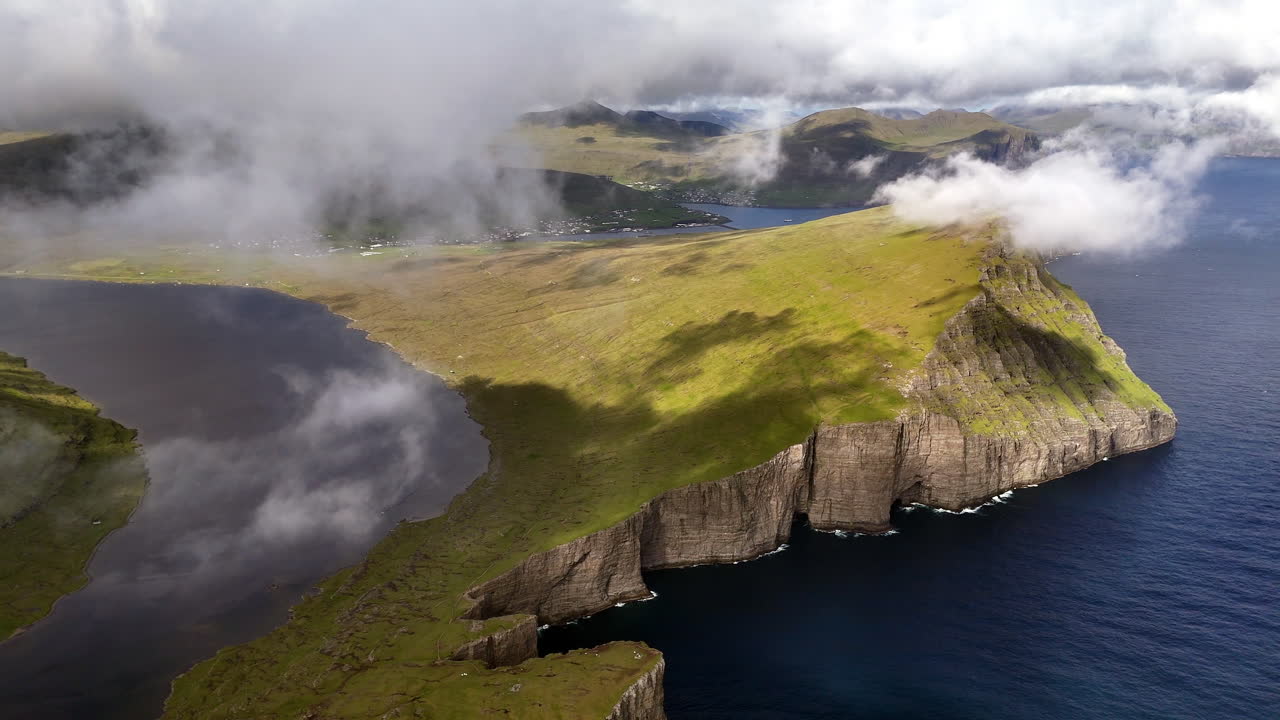 Aerial view of Lake Sørvágsvatn cliffs, Faroe Islands, with dramatic coastline, rolling clouds, rugged green slopes, and the Atlantic Ocean horizon, iconic Nordic landscape