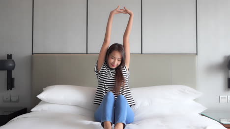 Beautiful-Slim-Casual-Asian-Woman-Sits-on-Bed-Stretching-Arms,-Static