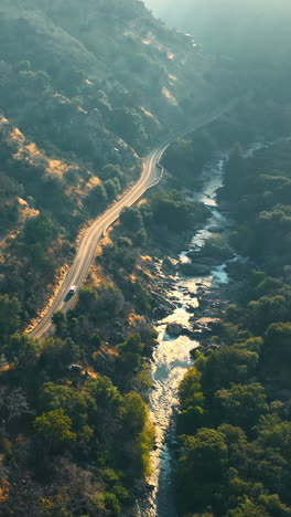 highway in the mountains along the narrow quick river. rocky landscape in the rays of setting sun. top view. vertical video