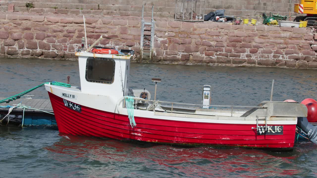 Small red fishing boat gently sways at harbor dock, daylight, steady camera, calm atmosphere