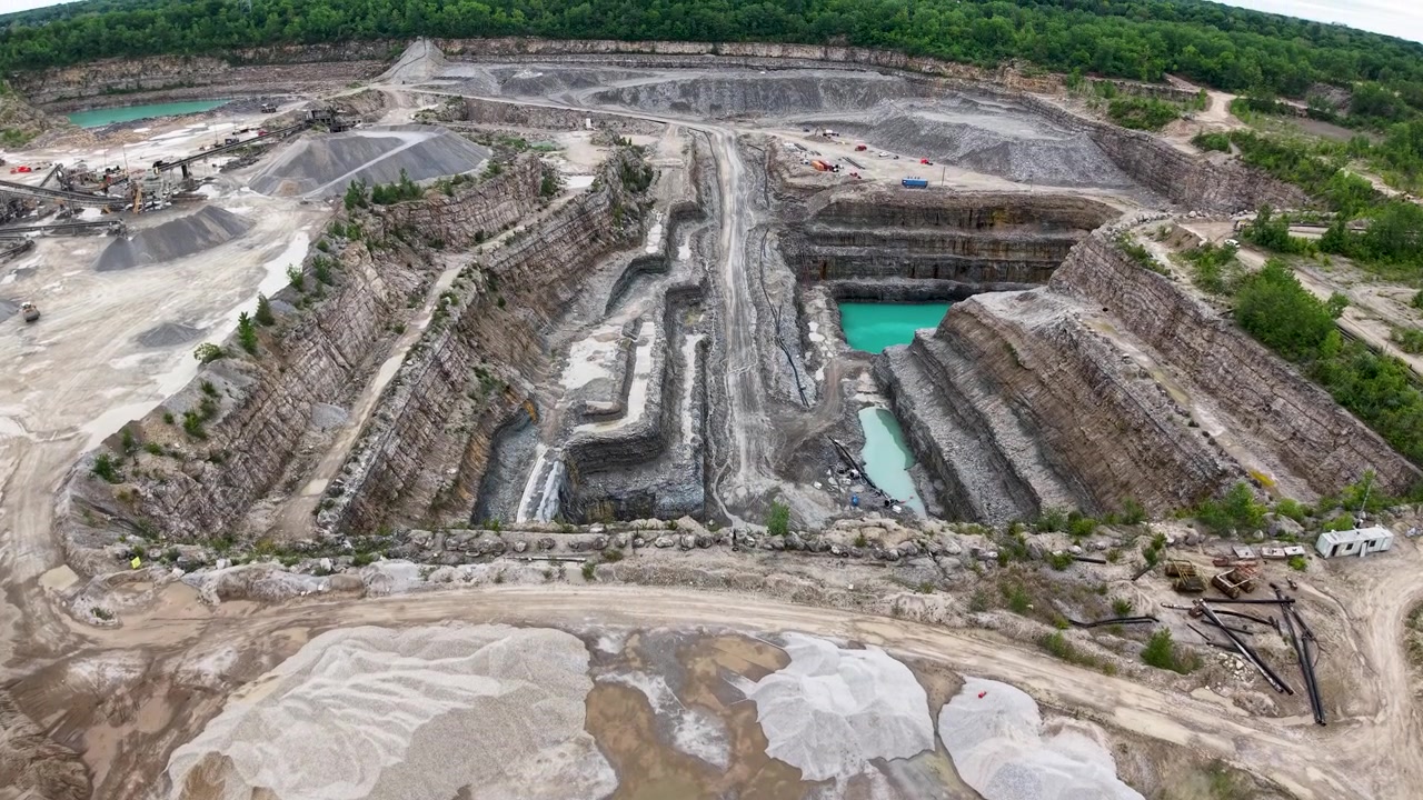 Vista aerea con drone su una cava a terrazze con una rampa di trasporto centrale e un bacino d'acqua turchese.