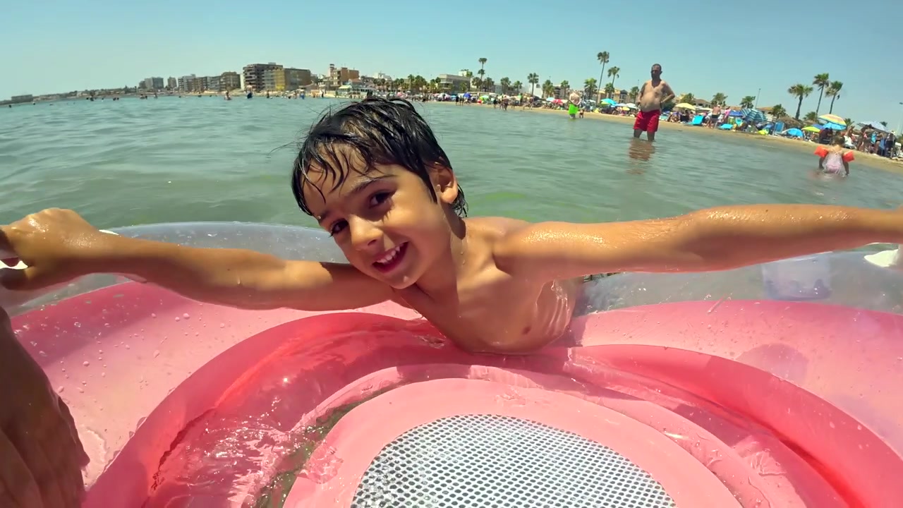 Happy Young Boy Playing on Pink Inflatable Ring at the Beach
