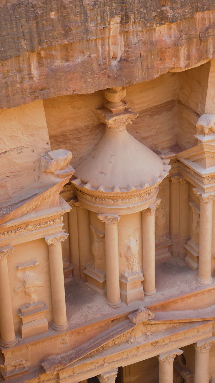 Primo piano verticale degli intricati intagli in pietra e dei dettagli architettonici ellenistici sulla facciata superiore di Al-Khazneh a Petra, Giordania