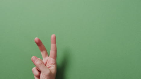 cerca de la mano de un hombre biracial que muestra un signo de paz con espacio de copia en un fondo verde
