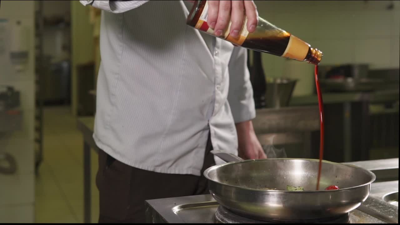chef vertiendo salsa de soja sobre las verduras en una sartén
