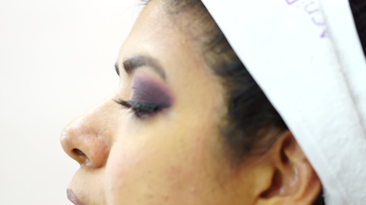 Side close-up of face of dark-haired woman fixing eyelashes with tongs