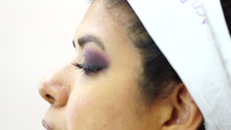 side close-up of face of dark-haired woman fixing eyelashes with tongs