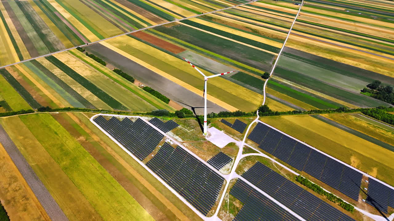 Fields with wind and solar. Aerial view of colorful agricultural fields featuring a wind turbine surrounded by solar panels on a sunny day
