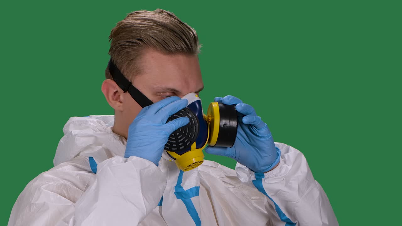 vista lateral de un médico de sexo masculino en un traje de protección blanco y guantes quirúrgicos pone un respirador médico. pantalla verde, tecla de croma. cámara lenta. primer plano