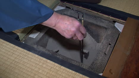 japanese tea master uses chopsticks to prepare ashes inside japanese shichirin charcoal stove