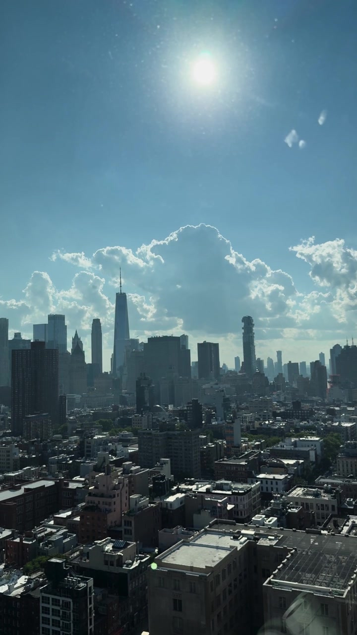 Bright midday sun over Manhattan skyline with scattered clouds and city buildings