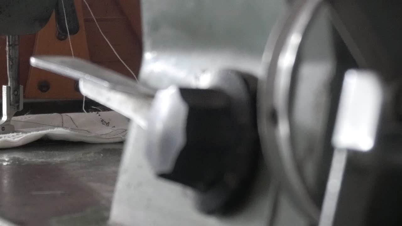 Smooth pan right shot of a vintage Refrey sewing machine stitching white fabric with green thread in a workshop setting