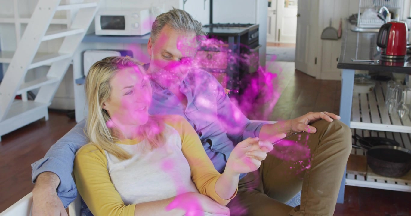 Coppia seduta sul divano che direziona particelle rosa con la mano in una spirale di nebbia che si dissolve, in una demo tecnologica.