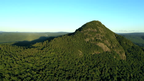 Aerial-drone-shot-pulling-away-from-Bore-Mountain-peak-at-sunset-above-thick-green-forest-trees-of-the-vast-Maine-wilderness