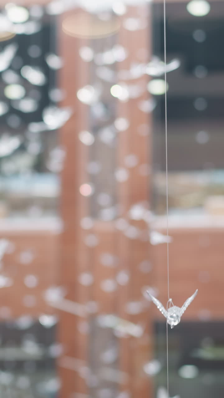 Blurred view of a reflective glass surface in a modern mall, featuring a suspended decorative object shaped like a bird in focus, with a dynamic bokeh effect of light in the background