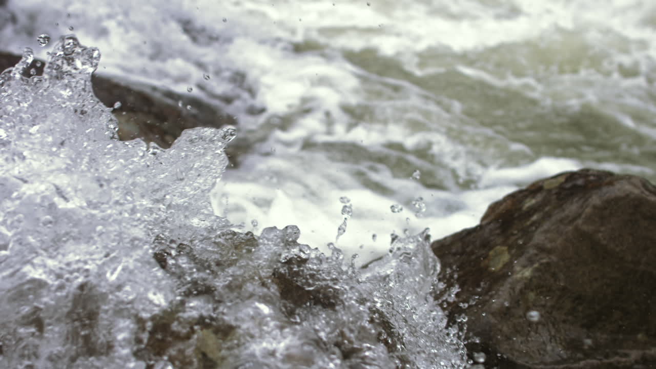 Close up slow motion fast moving water splashing up against a rock in a rapids in Suck Creek in Chattanooga, Tennessee.