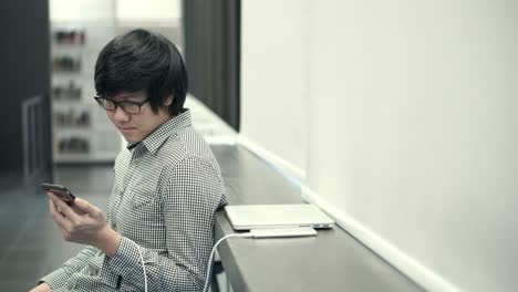 young asian business man using smartphone on social media application while charging device. urban lifestyle in working space concept.