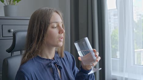 girl drinking clear water from glass, while working in home office