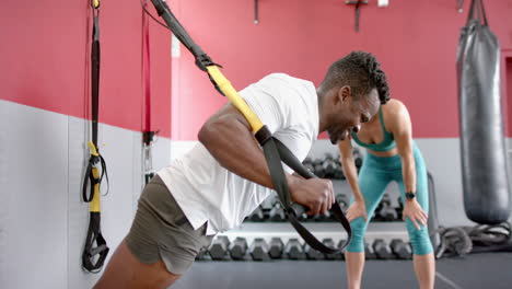 Un-Hombre-Afroamericano-En-Forma-Entrena-A-Una-Joven-Caucásica-En-El-Gimnasio.