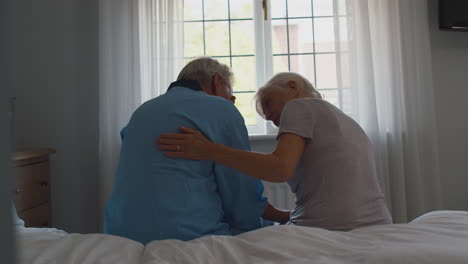 worried retired senior couple sitting on bed at home talking together